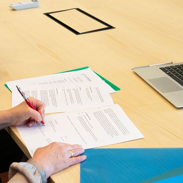 En person skriver under avtal, datorn framför henne visar flera andra personer göra detsamma.