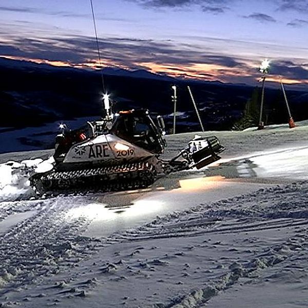 Pistmaskin preparerar skidbacke i Åre under skymningen med berg i bakgrunden.