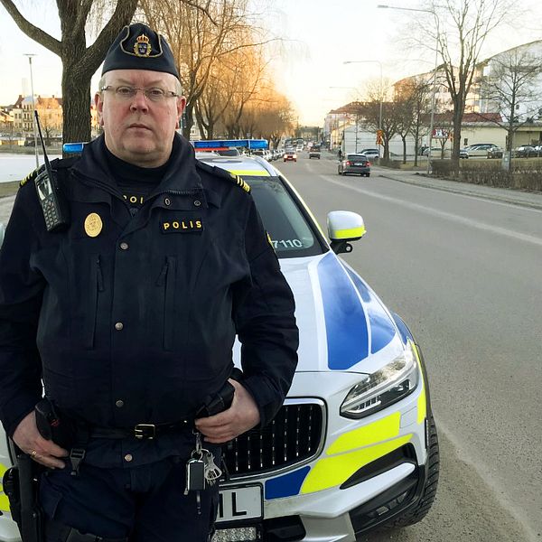 Porträttbild på polisen Erling Arvidsson som står framför en polisbil utmed en bilväg.