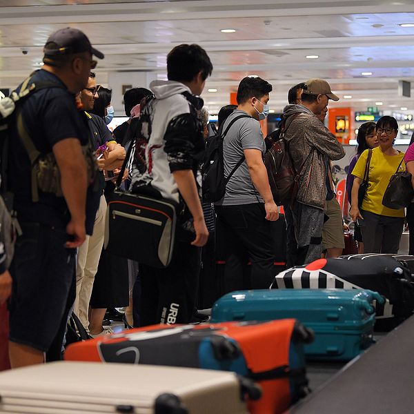 Personer står och väntar på bagage på flygplats.