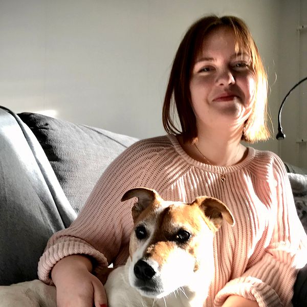 Amanda Wall i rosa tröja sitter i en grå soffa med en liten brunvit hund.