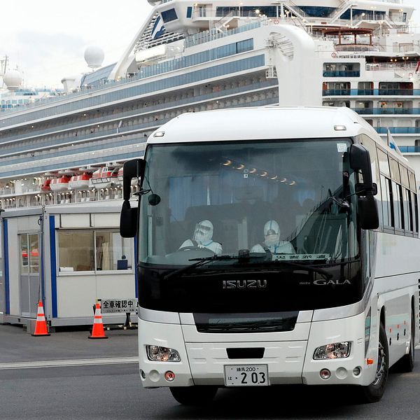 En buss med passagerare som varit ombord på Diamond Princess får lämna hamnen i Yokohama i Japan. I bakgrunden syns fartyget.