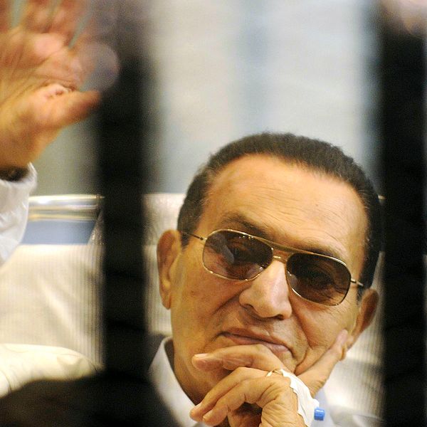 Den tidigare presidenten, Hosni Mubarak, bärandes på solglasögon vinkar medan han är bakom galler.