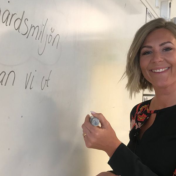 Kvinna skriver på whiteboard-tavla i klassrum.