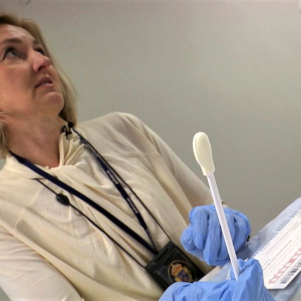 Kvinna med blåa gummihandskar har en DNA-tops i handen.