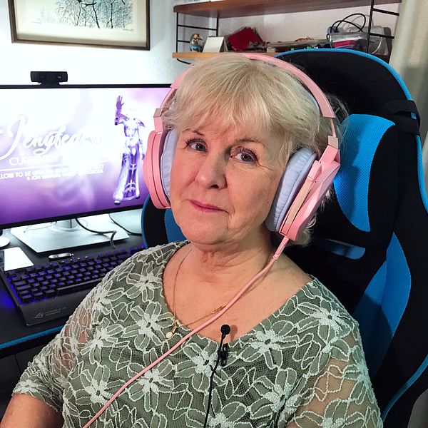 Äldre kvinna med hörlurar framför datorn.
