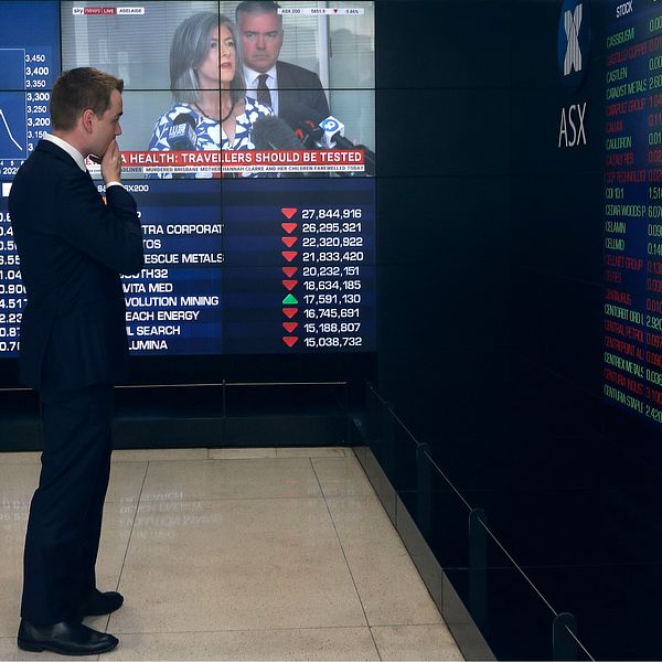 En man tittar på stora skärmar som visar siffror från börsen.