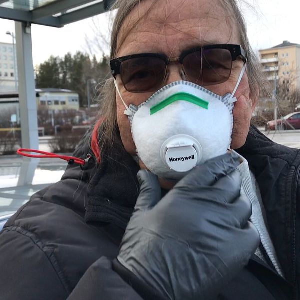 Man som är högriskpatient med munskydd och svarta handskar utanför sjukhuset i Umeå