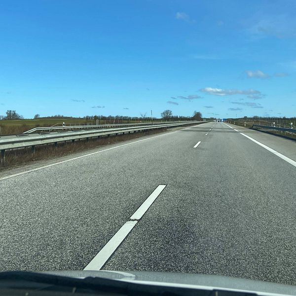 Bild tagen innifrån en bil, man ser en tom väg och blå himmel.