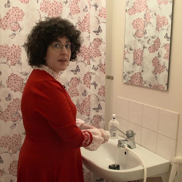 Kvinna i röd klänning tvättar händerna i badrum