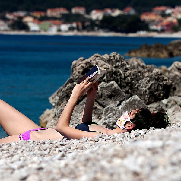 En ensam kvinna i munskydd som solbadar på en strand på Cres i Kroatien. Tidigare år har stranden varit full med människor den här tiden på året.