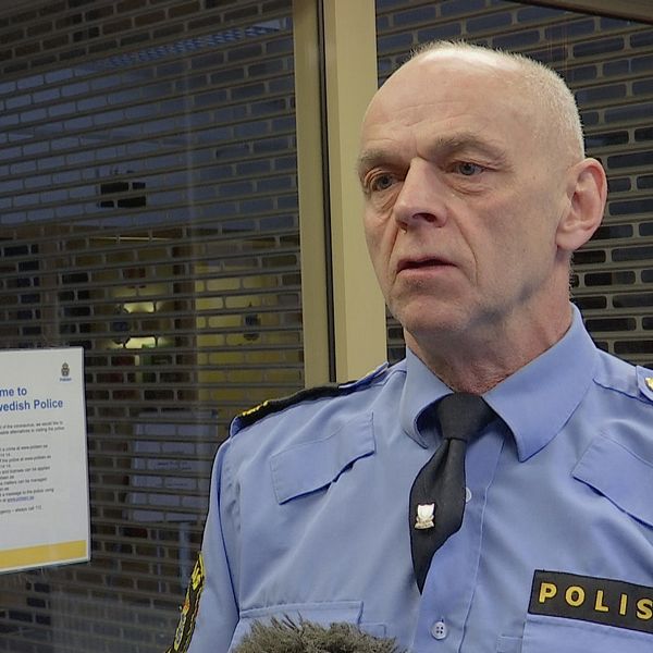 en äldre man i polisskjorta intervjuas i korridor i polishuset