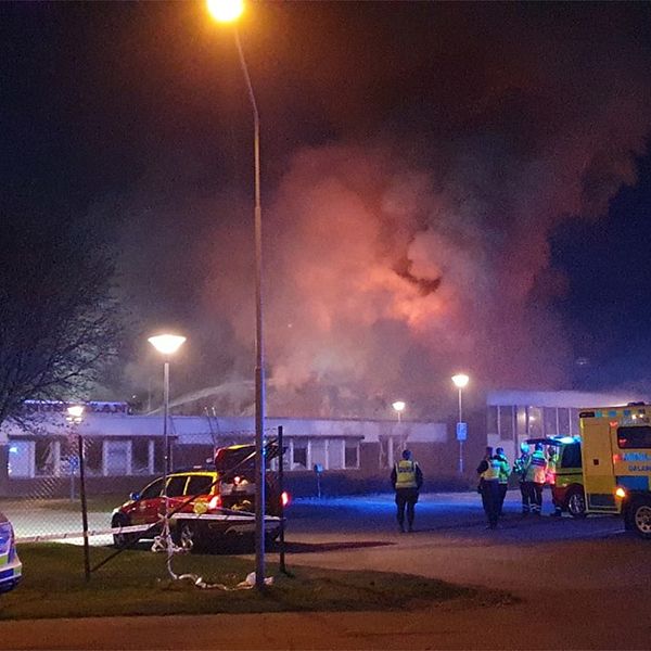 Ambulans och polisbil syns utanför en skolbyggnad. Det ryker kraftigt från byggnaden.