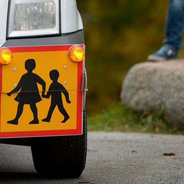 närbild på skylt på en skolskjuts-bil, i bakgrunden syns fötterna på en pojke som står på en sten