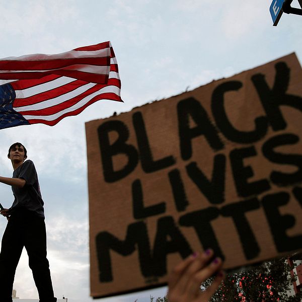 Ung man vajar USA:s flagga. En skylt med texten ”Black lives matter” syns också.