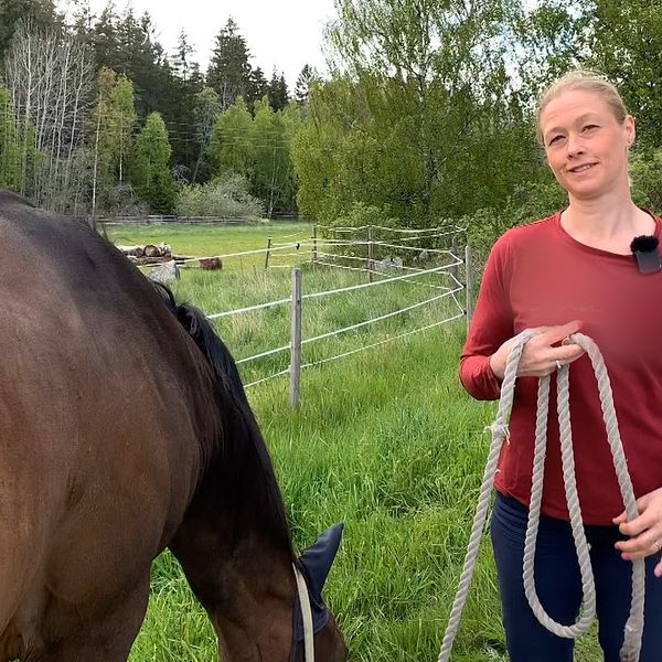Annelie Manberger står på en väg med häst i grimskaft. Det är sommar och gröna hagar syns i bakgrunden.