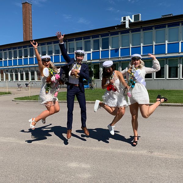 Fyra studenter, Liza Bergström, Elias Rahm, Jasmine Engström och Emma Törnevik, som hoppar av glädje framför en skolbyggnad.