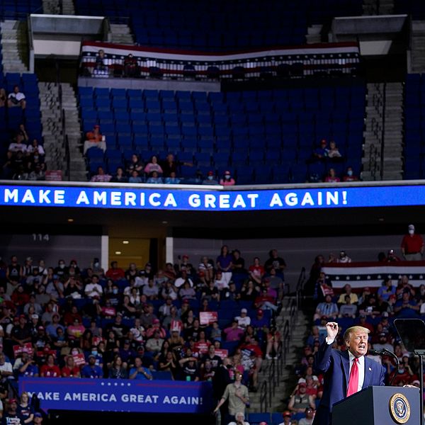 Donald Trump står vid talarstolen på scenen i en stor arena med halvtomma läktare.