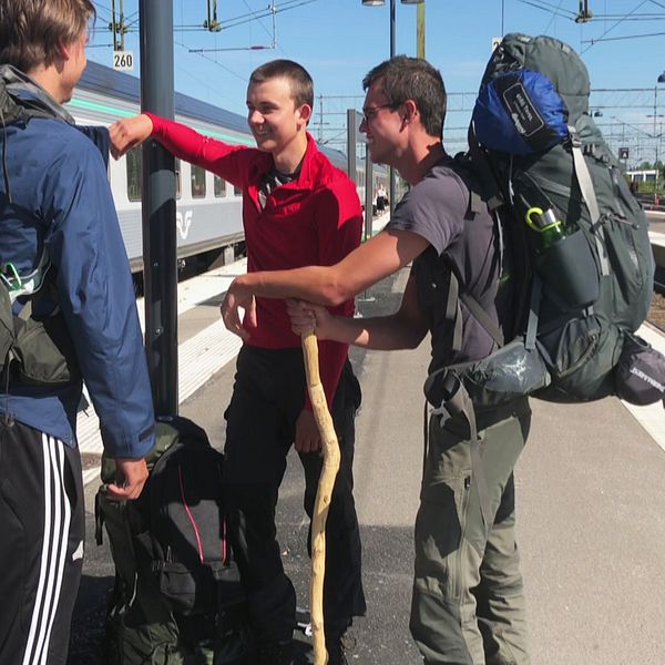 tre killar med ryggsäck utanför tåg på perrong
