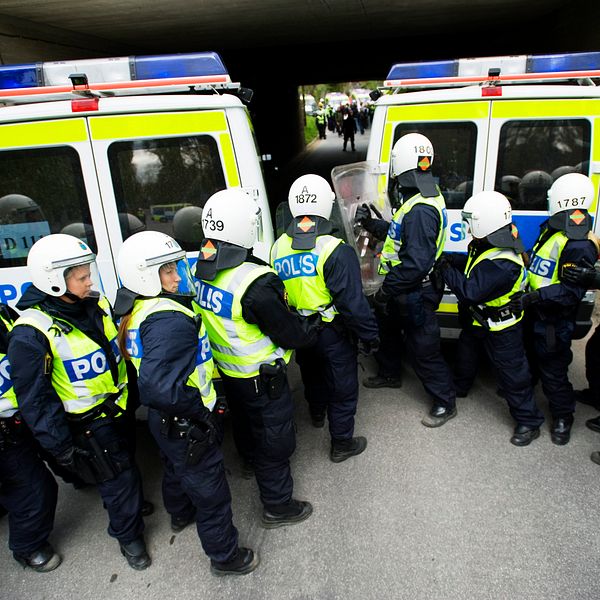 Polisstudenter övar med hjälm och skyddsväst framför två pikébussar.