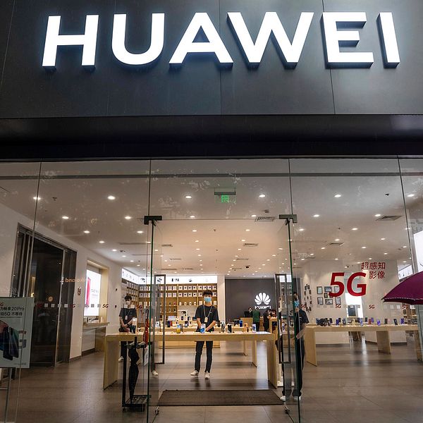 Bild tagen underifrån. En man med munskydd och paraply passerar skyltfönstret på en Huawei-butik.