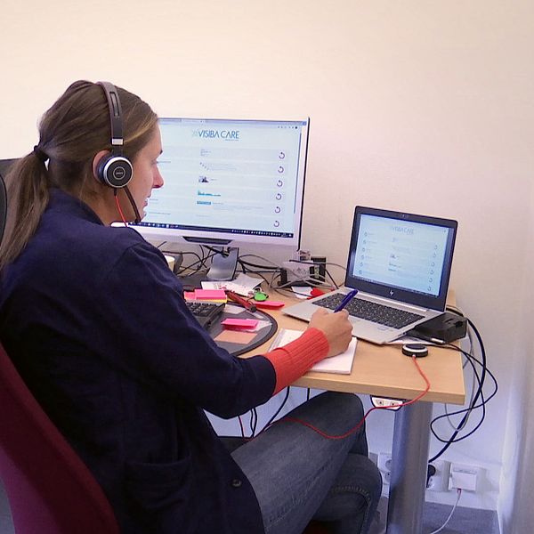 En kvinna sitter framför två datorer med ett headset och arbetar.