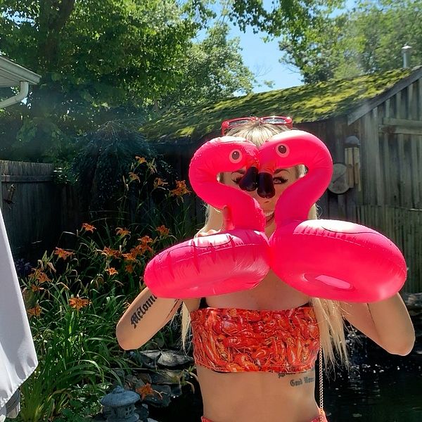 Artisten Jasmine Kara står i bikini och håller upp två rosa plastflamingos, som bildar ett hjärta, framför ansiktet.