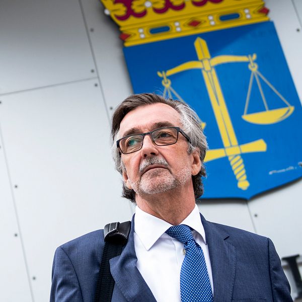 försvarsadvokat Gunnar Falk står framför domstolssymbolskylt med vågskålar