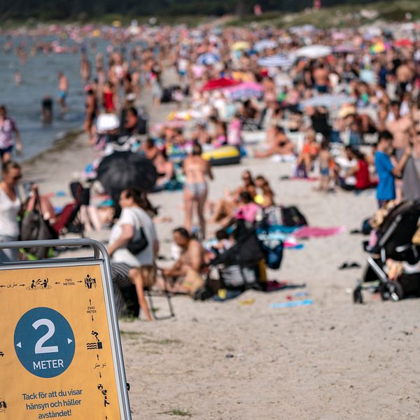 En skylt påminner om att hålla avstånd på stranden i Lomma, Skåne. Polisen i Sverige har fått in många samtal om trängsel på badstränder.