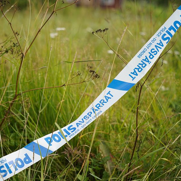 Ett polisavspärrningsband knutet i lyktstolpe har ramlat ner i gräset vid brottsplatsen