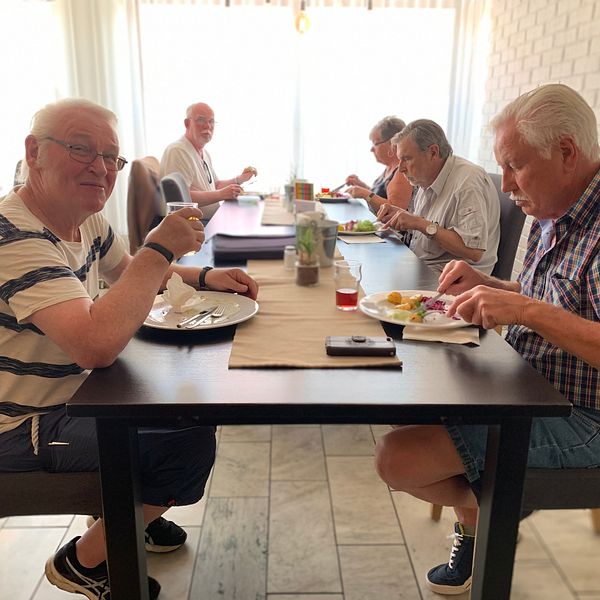 Hjalle sitter vid ett lunchbord på en restaurang tillsammans med sina vänner. Han tittar mot kameran och ler.