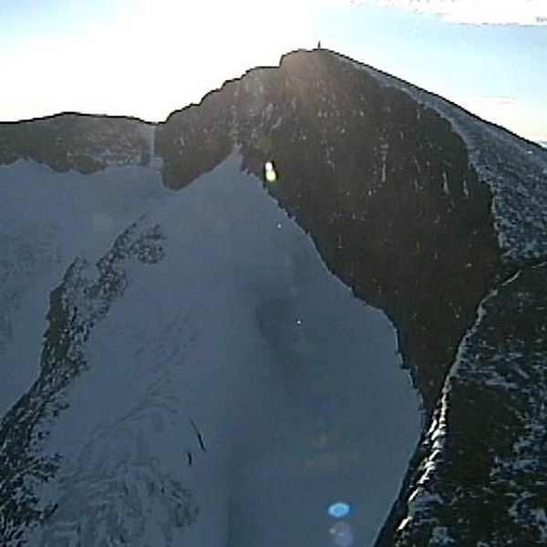 flygbild på bergstopp med brant sida med glaciär nedanför