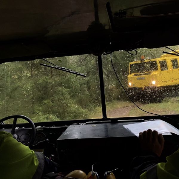 Sikt ut från en bandvagn som möter en likadan gul bandvagn på en skogsstid.