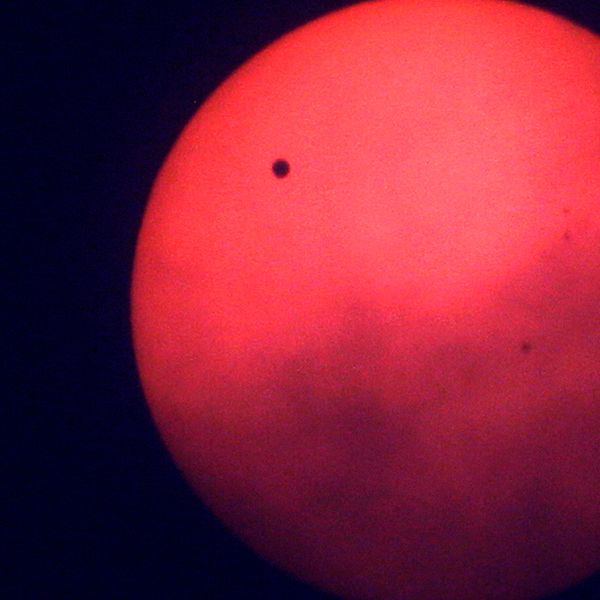 En bild på planeten Venus som lyser rött ute i den mörka rymden.