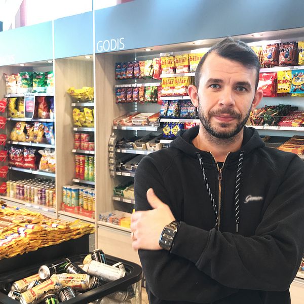 Richard Björkman står med armarna i kors i sin kiosk i stationshuset. I bakgrunden syns långa hyllor med chips, läsk och godis.