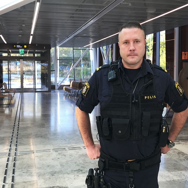 Polisen Peter Sigurd står med händerna på höften i resecentrum i Strängnäs. I bakgrunden syns informationstavlor, bänkar och glasrutor.