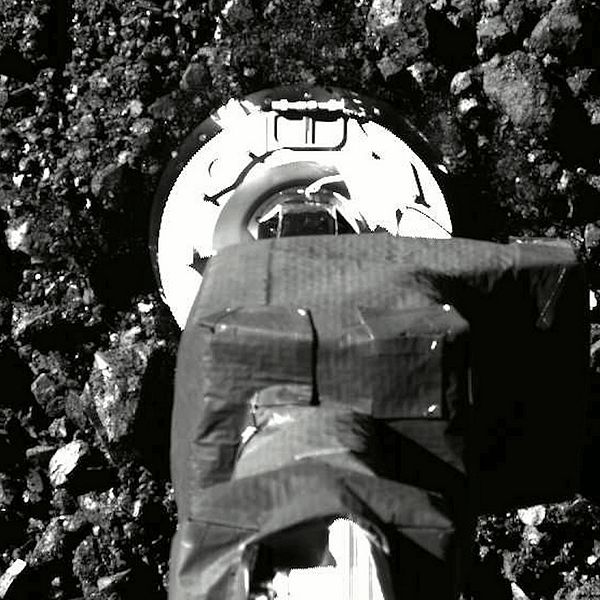 En svartvit bild på rymdsondens fot då den landat på asteroiden Bennu.