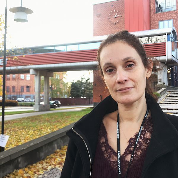 Biljana Sekaric står framför den långa trappan vid Rinmangymnasiets huvudentré. I bakgrunden syns även gångbron över vägen med texten ”Rinmangymnasiet” i stora gråa bokstäver.