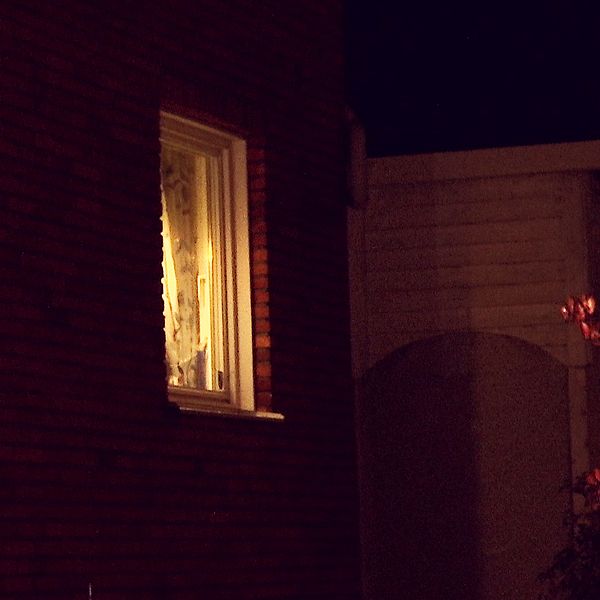 Ett tegelhus i mörker med ett fönster som det lyser i.