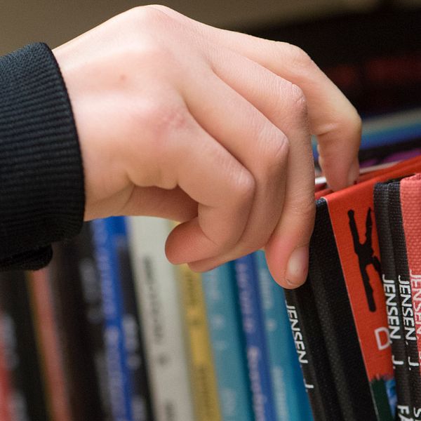 En hand plockar ut en bok från en bokhylla.