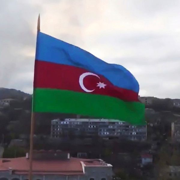 Azerbajdzjans flagga med staden Sjusji i bakgrunden, i den separatistiska regionen Nagorno-Karabakh. I bakgrunden syns även rök.