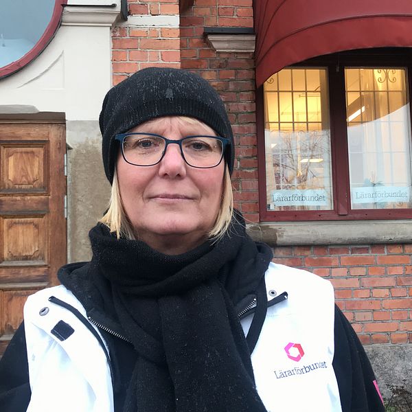 Cecilia Rahbek Nöhr står i regnet utanför Lärarförbundets lokal i Eskilstuna, den gamla busstationen i rött tegel. Hon har regn på glasögonen och en vit väst med texten ”Lärarförbundet” på.