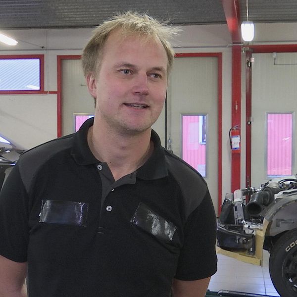 Joel Christoffersson i sitt garage med rallycrossbilar i bakgrunden.