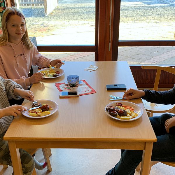 Tre elever sitter vid ett bord i skolmatsalen.