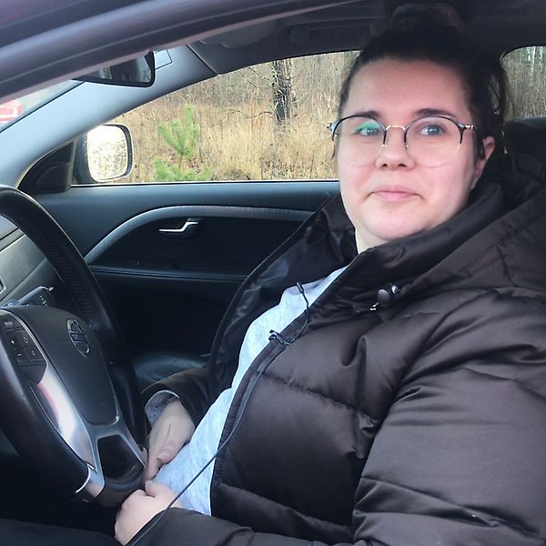 Julia sitter i sin bil, iklädd svart vinterjacka och glasögon.