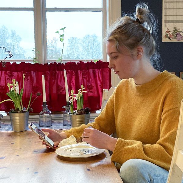 Mira Åslin äter en smörgås och tittar på sin mobiltelefon.