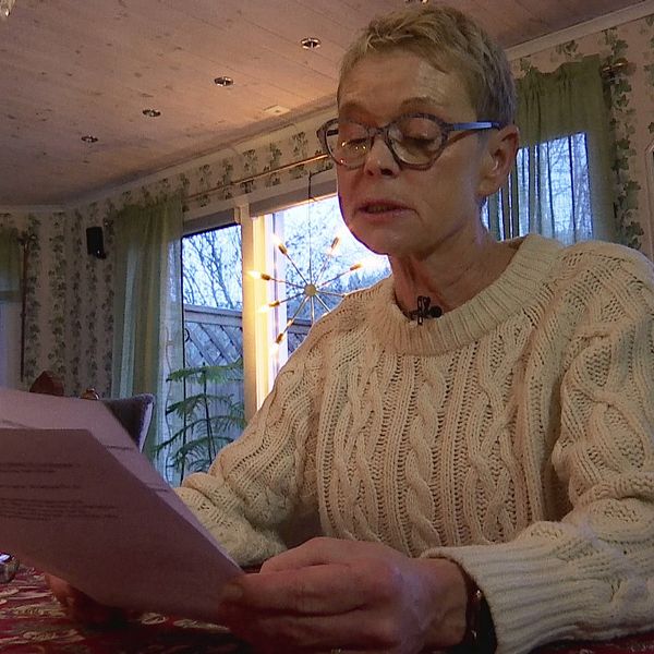 Elisabeth sitter i sitt vardagsrum och läser i ett papper. Hon ser bekymrad ut.