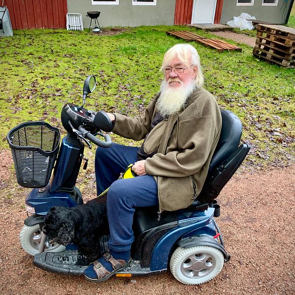 en äldre man i trehjulig elrullstol med styre, ute på sin gård