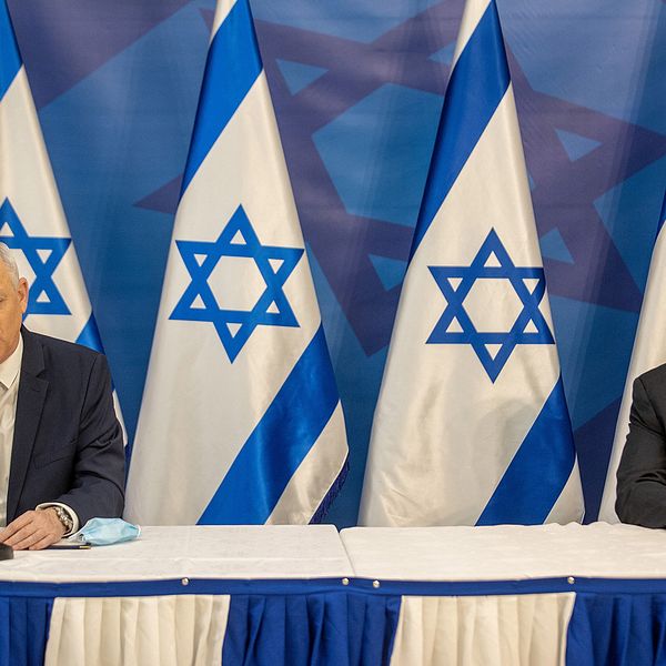 Benny Gantz och Benjamin Netanyahu sitter med två meters avstånd till varandra under en presskonferens med fem israeliska flaggor bakom sig.