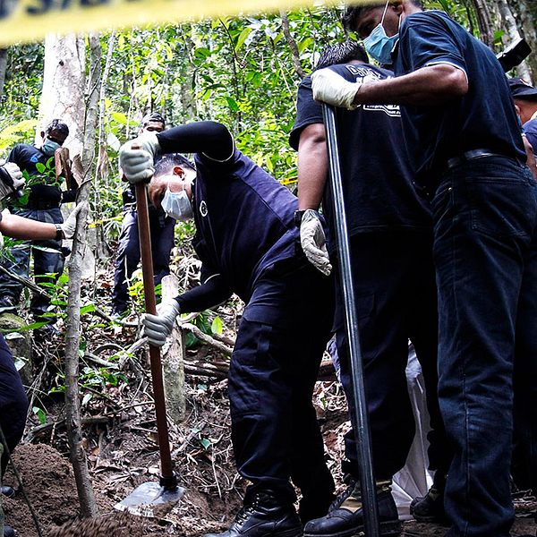Malaysisk polis undersöker några av de gravar som upptäckts nära thailändska gränsen.